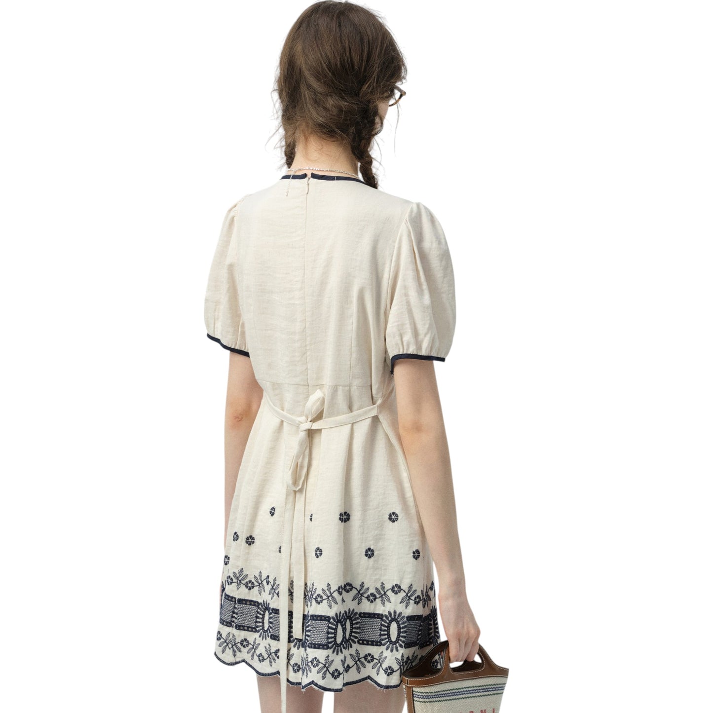 フレンチシックな刺繍ワンピースを着た女性の横からのショット。ふんわりとしたパフスリーブと流れるようなスカートのシルエットが美しい。